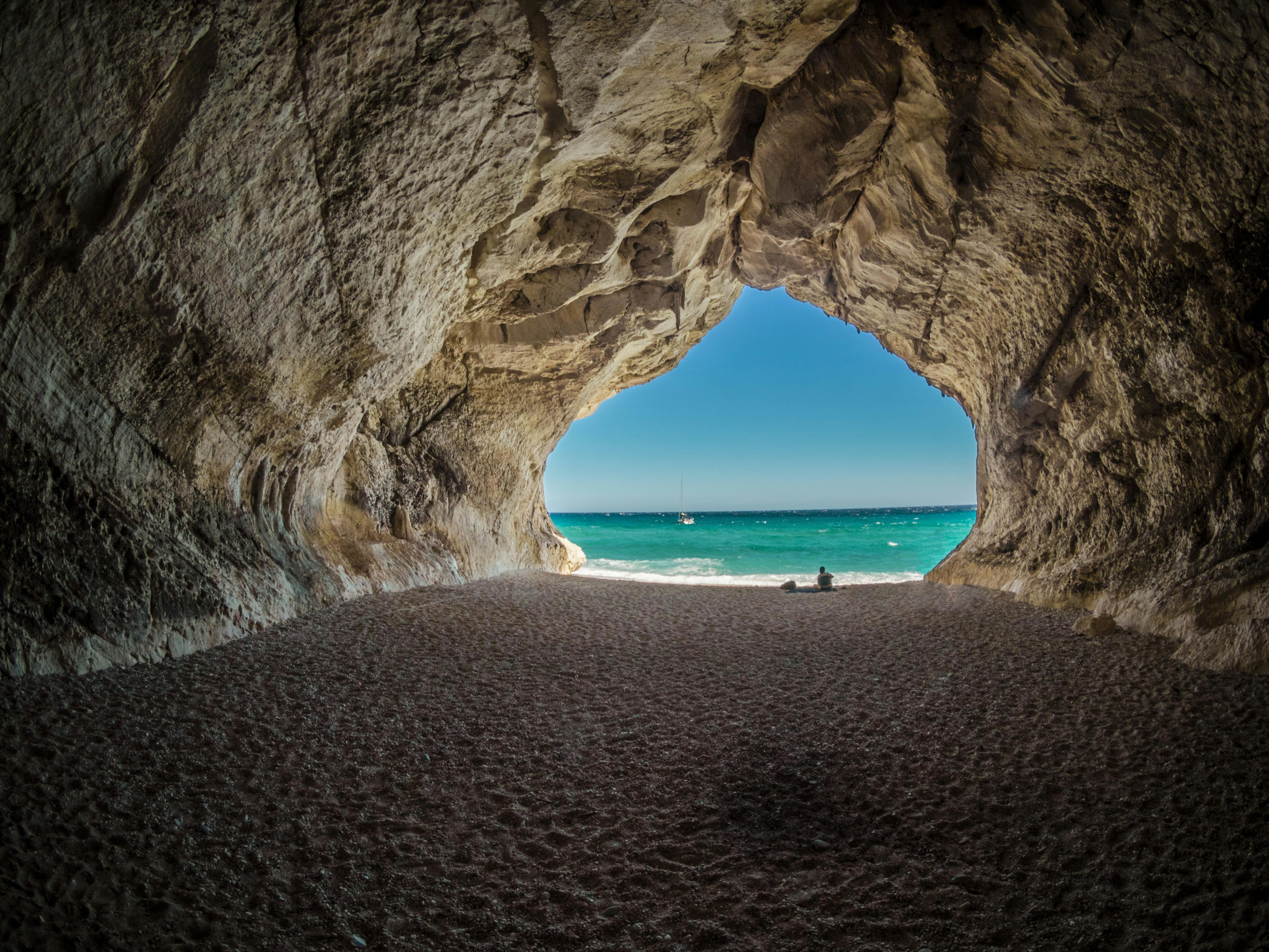 A cave opens out to a beach and the ocean, with a person on the sand