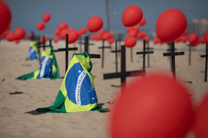 Crosses, red balloons and Brazilian nation flags appear on a beach in a demonstration to remember Brazil's coronavirus victims.