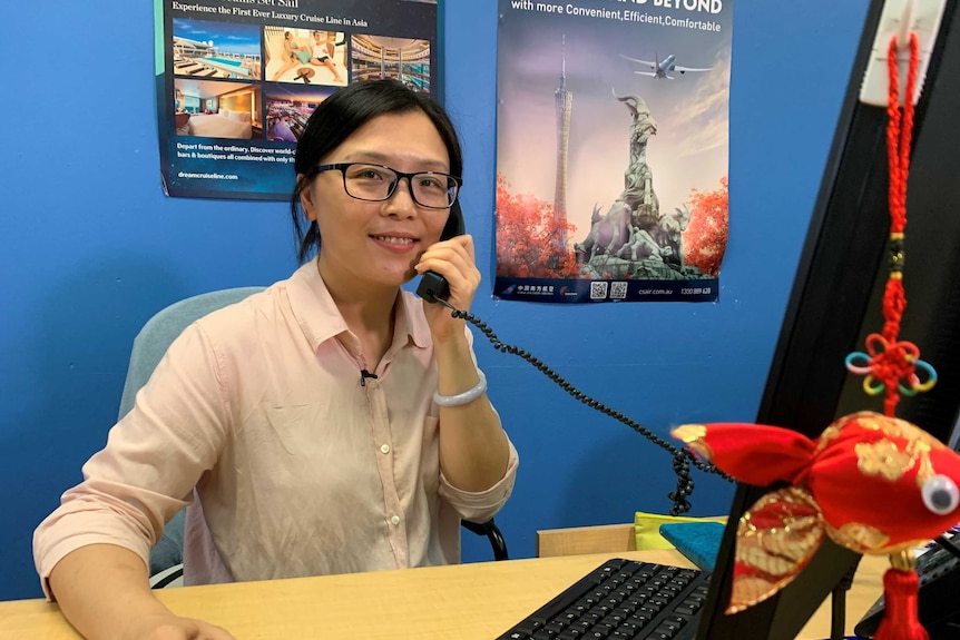 A woman sitting at a desk on the phone smiling at the camera