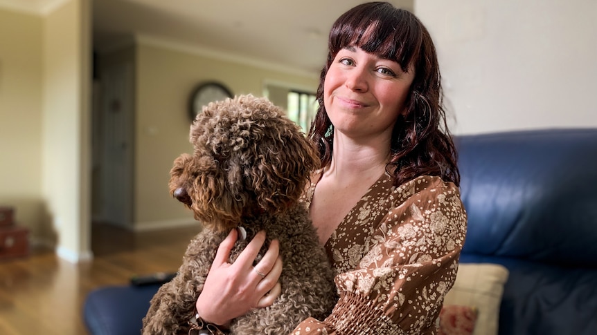 A woman in a brown dress holds a brown poodle on her lap