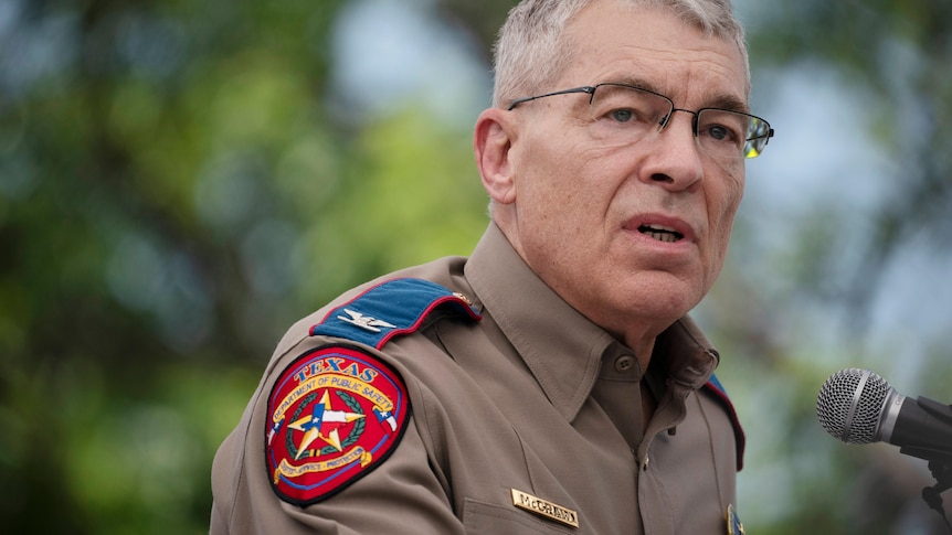 A Texas police office gives a press conference wearing a brown shirt with a red patch on the sleeve