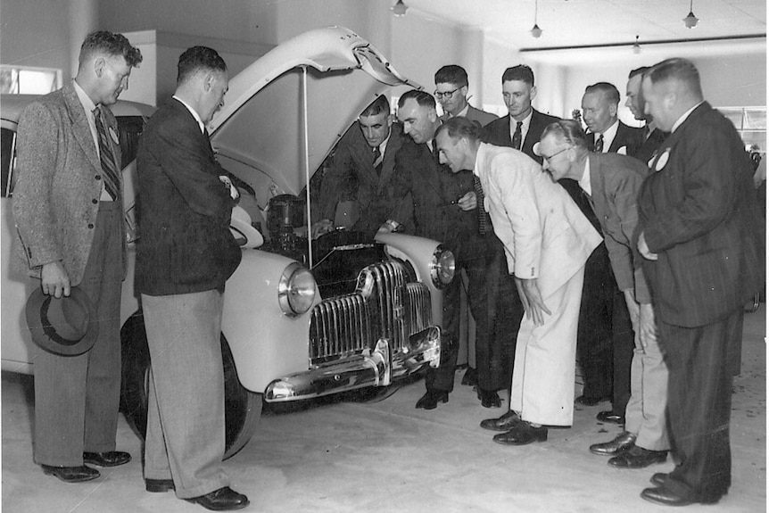 A black and white photo of men in the 1940s wearing suits, standing around inspecting a Holden