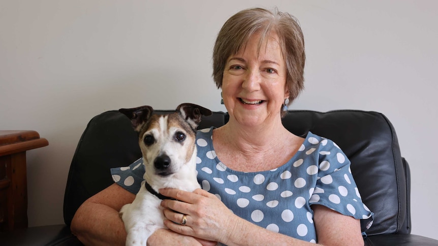 A woman sitting on a chair smiling with a dog in her lap.