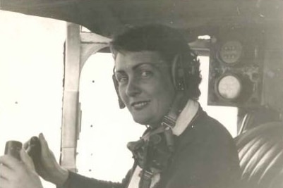 A black and white photo of a woman in the cockpit of a plane with hands on the controls