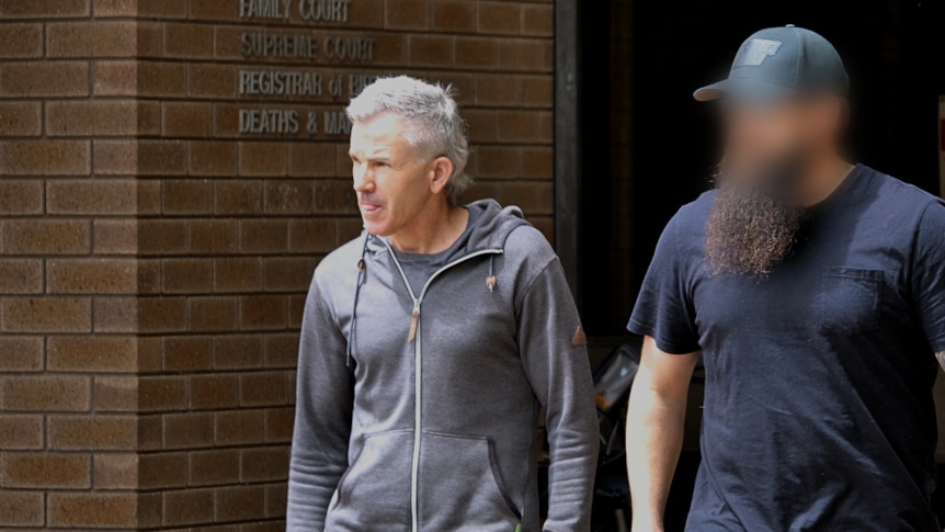 A man with grey hair walks out of a brick court building.