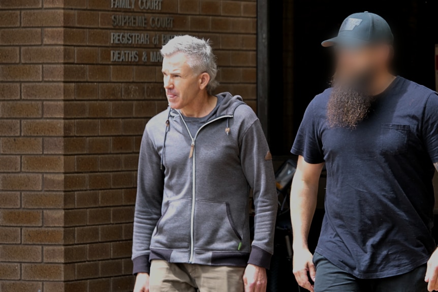 A man with grey hair walks out of a brick court building.