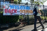 a young student walking outside his school gates with a banner that reads welcome back to school