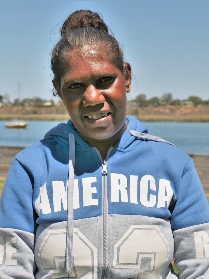 A lady smiles at the camera in front of a body of water.