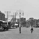 A black and white photo of a historic streetscape with a man riding down the middle on a bicycle 
