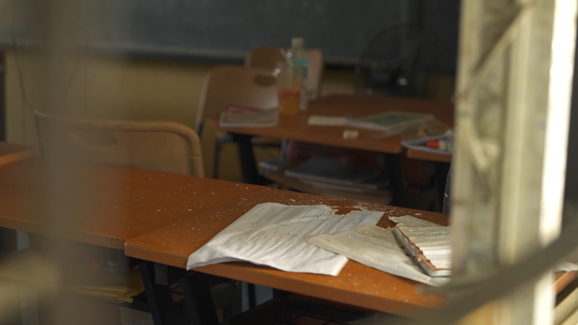 A dimly lit classroom with wooden school desks and chalkboard sits empty.