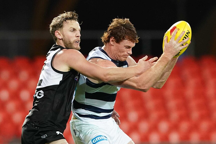 An AFL forward holds ball in two hands after taking a mark inside forward 50 in front of a defender.