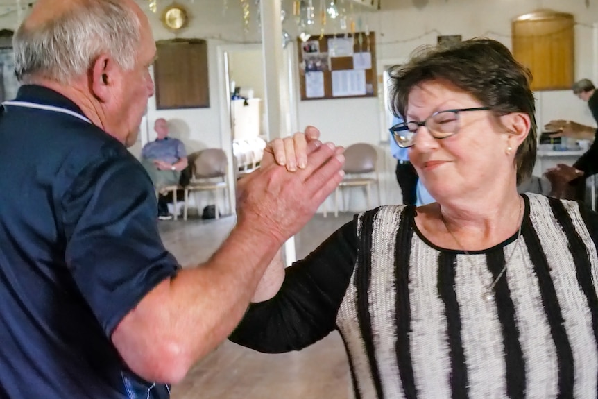A older man in a blue polo shirt dances with a woman in a striped top.