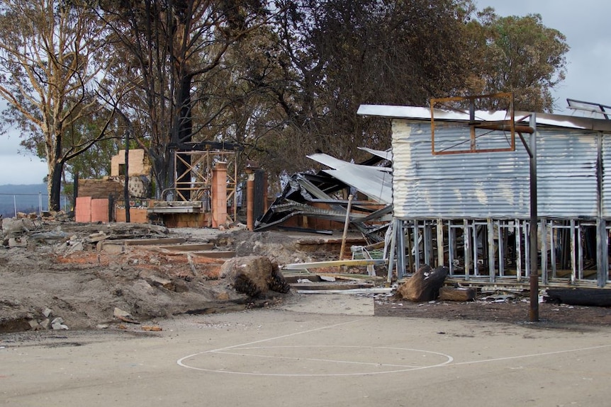 The basketball backboard and ring are burnt out, only the metal pole and frame remain. Burnt out buildings are in the background