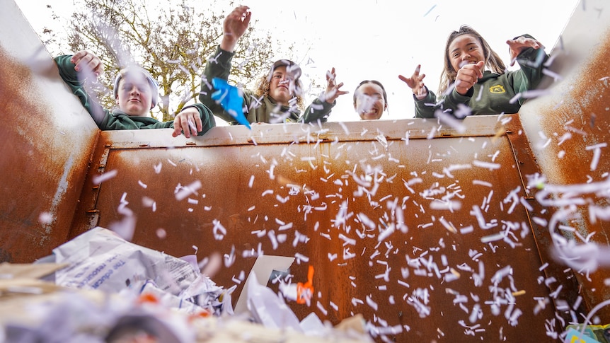 Four teenage students throw shredded paper into a skip bin, creating a falling snow affect.