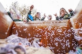 Four teenage students throw shredded paper into a skip bin, creating a falling snow affect.