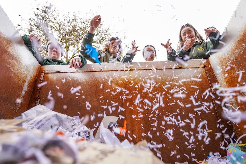 Four teenage students throw shredded paper into a skip bin, creating a falling snow affect.