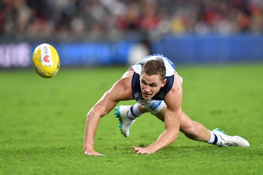 Joel Selwood slips on the ground as he looks at the ball in front of him.