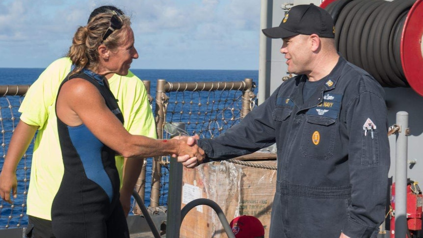 Jennifer Appel stands on a boat and shakes hands with USS Ashland Command Master Chief Gary Wise.