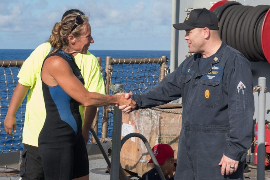 Jennifer Appel stands on a boat and shakes hands with USS Ashland Command Master Chief Gary Wise.