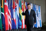 Xi walks in suit and waves in front of line of world flags