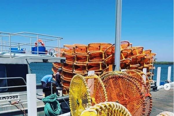 Crab pots stacked on a jetty, being loaded onto a fishing boat by workers.