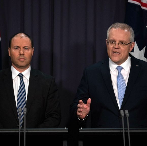 two men in suits in front of two australian flags