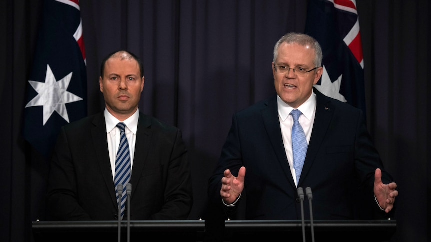 two men in suits in front of two australian flags