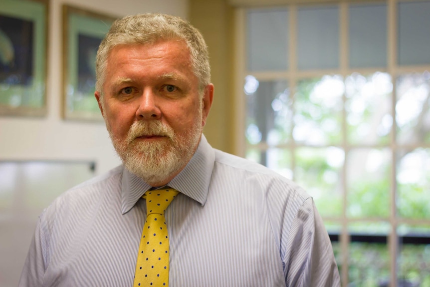 A man wearing a yellow tie stands in an office