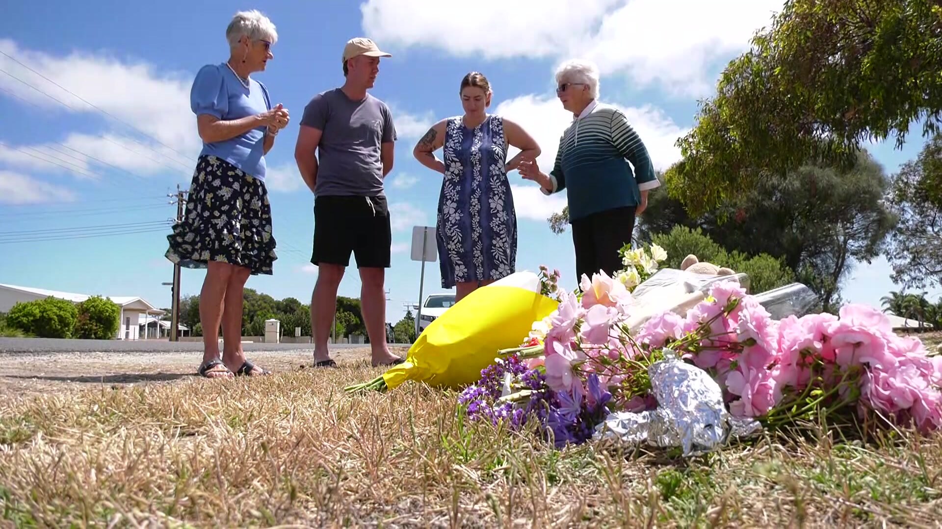 People gather around floral tributes.