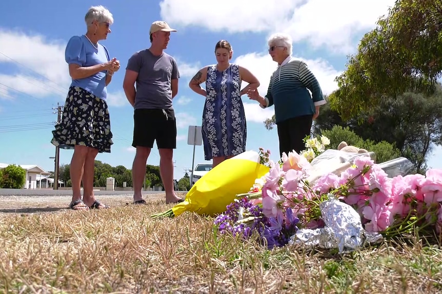 People gather around floral tributes.