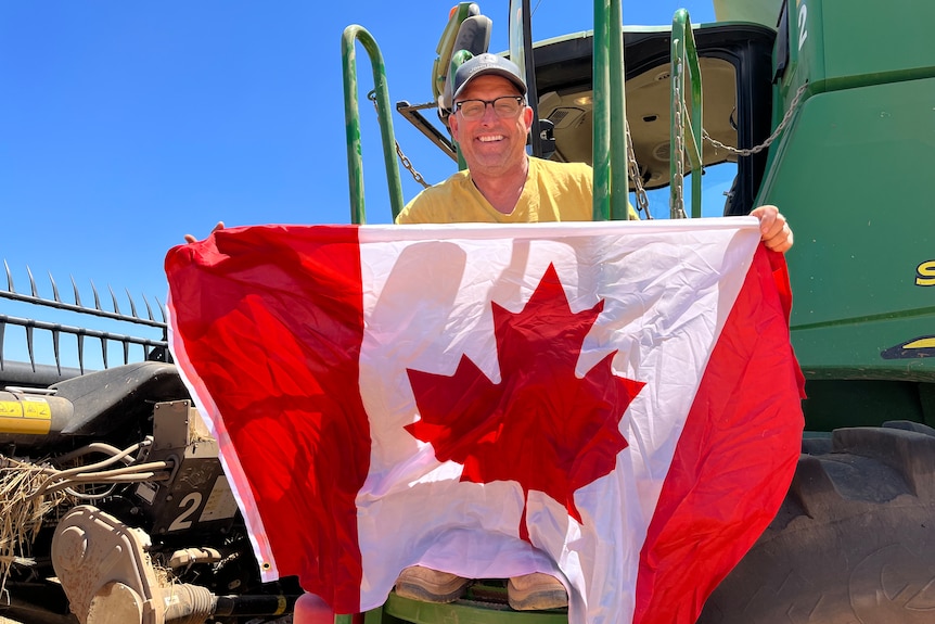 Craig Ozipko is holding a Canadian flag outside his grain harvester