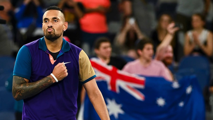 Nick Kyrgios pumps his fist against his chest with an Australia flag in the background