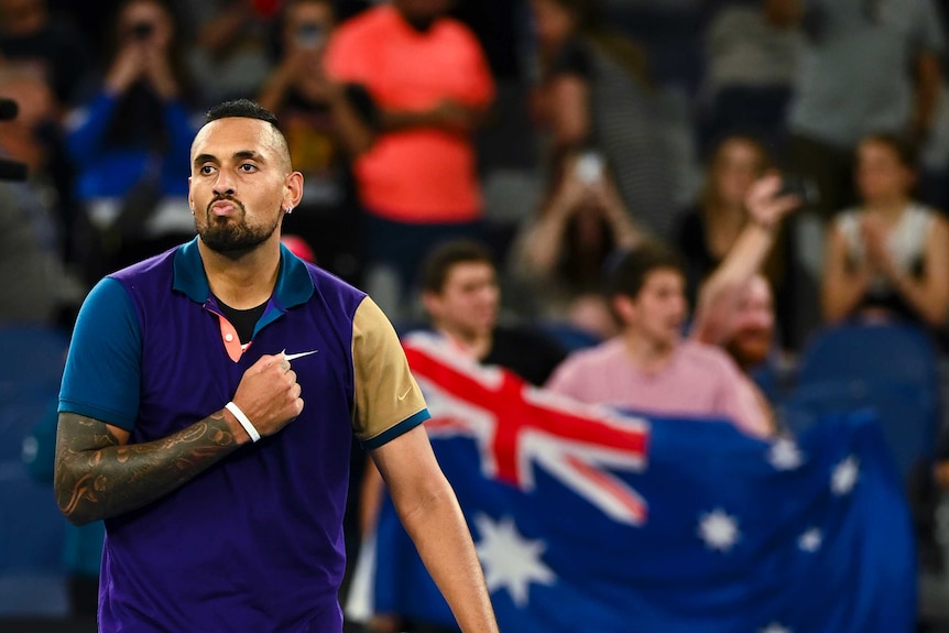 Nick Kyrgios pumps his fist against his chest with an Australia flag in the background