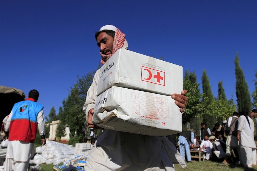 An Afghan man carries a box with the Red Cross insignia on it
