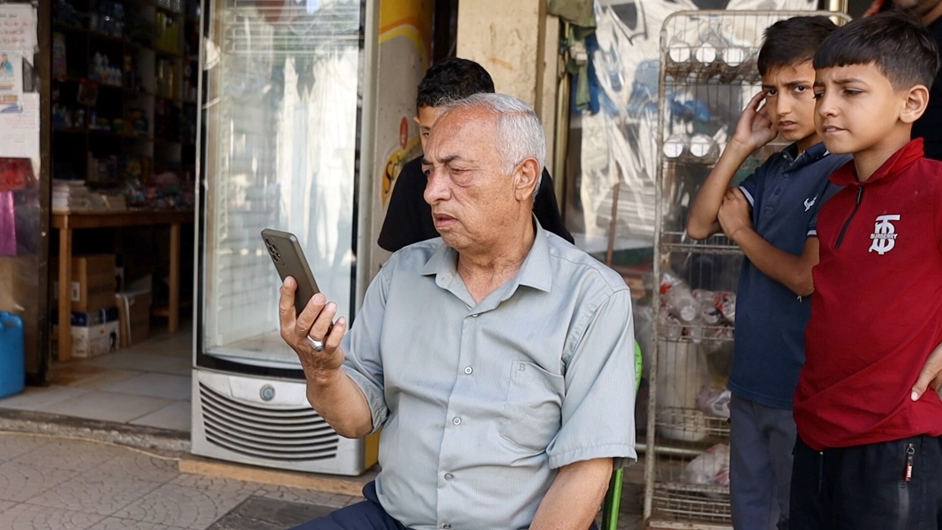 A man looks at a mobile phone, two children are standing behind him. 