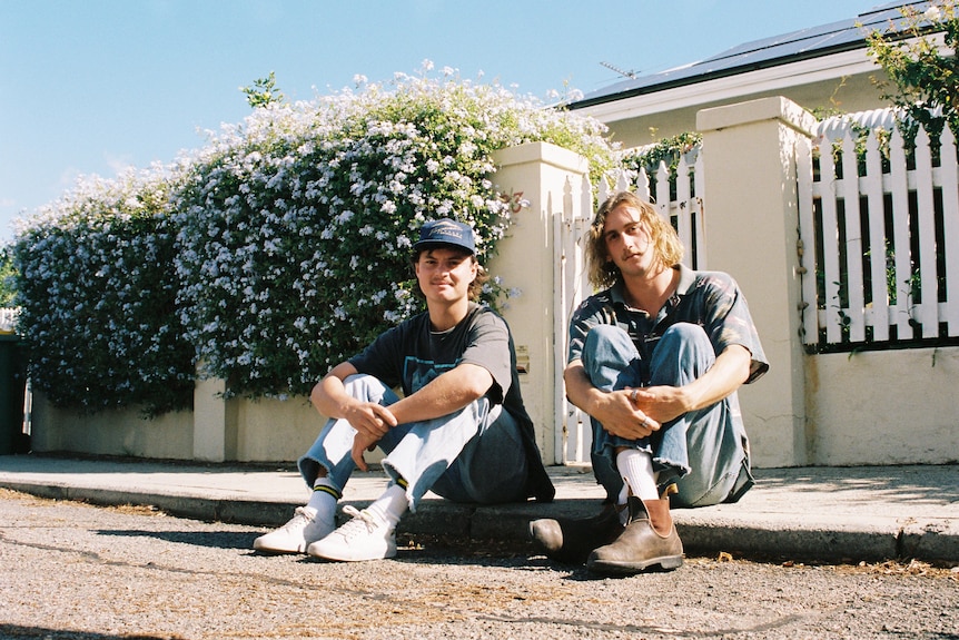 Two men sitting on sidewalk.