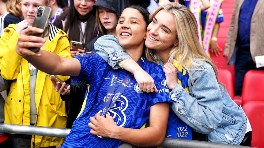 A soccer player wearing blue and yellow takes a photo with her girlfriend after a match