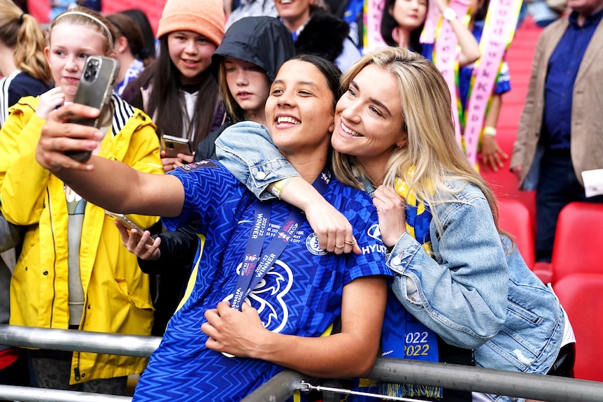 A soccer player wearing blue and yellow takes a photo with her girlfriend after a match