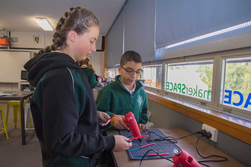 A girl and boy using hot glue guns in a school classroom