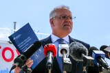 Morrison holds up a printed policy paper in front of a bank of microphones