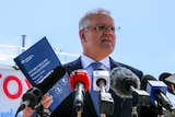 Morrison holds up a printed policy paper in front of a bank of microphones