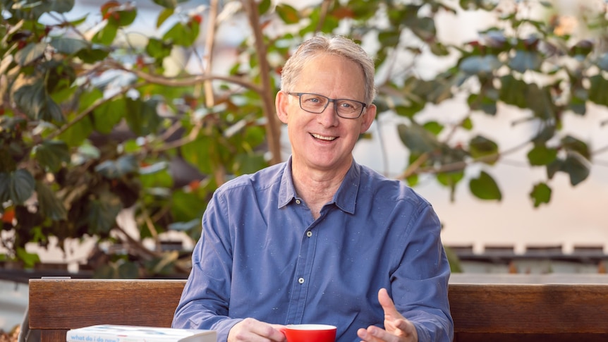 Man with a blue shirt sits at a cafe table smiling at the camera