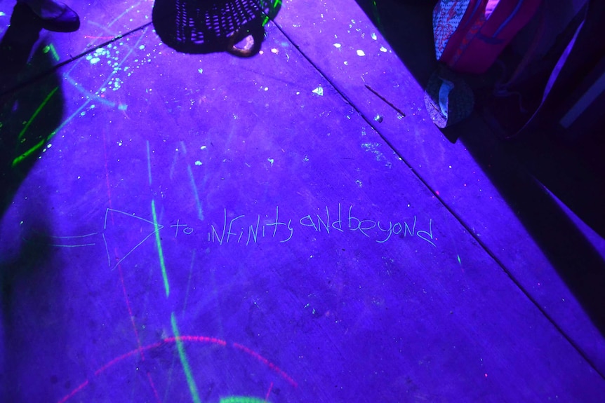 "To infinity and beyond" written in neon paint on the floor at Julian Scharf's party.