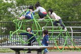 Kids in face masks climb over playground equipment