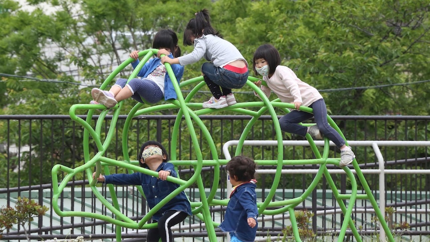 Kids in face masks climb over playground equipment