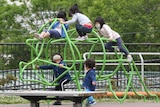 Kids in face masks climb over playground equipment