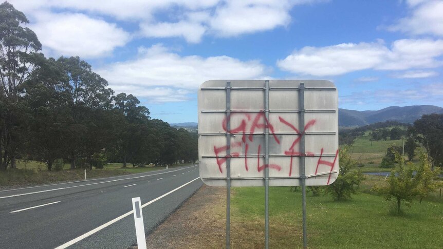 The back of a square street sign with the words "gay filth" spray painted on in red