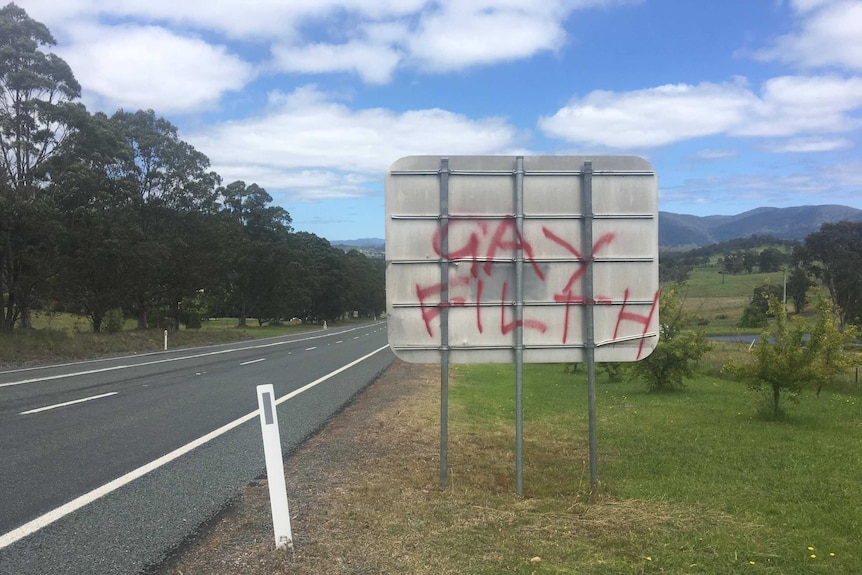 The back of a square street sign with the words "gay filth" spray painted on in red