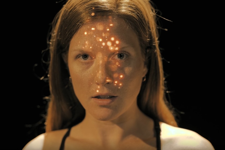 A young woman stares at the camera, sparkles of light projected on her face