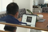a man sitting behind a computer at a dining room table at home